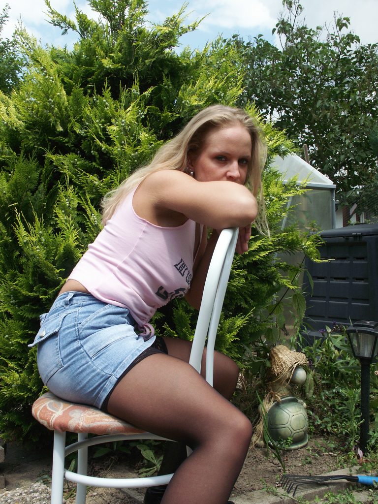 Junge Blondine in Hotpants und Strumpfhosen sitzt im Garten auf einen Stuhl